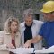 Courtier en travaux présentant les plans du chantier à un couple de propriétaires