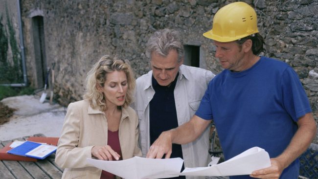 Courtier en travaux présentant les plans du chantier à un couple de propriétaires