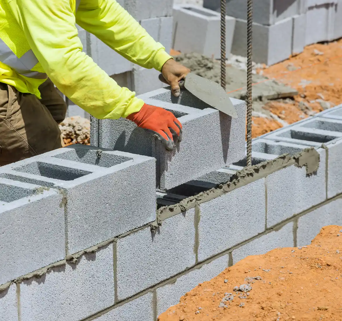 Extension en maçonnerie traditionnelle Maçon montant un mur en parpaings creux avec fers de chaînage sur un chantier d'extension